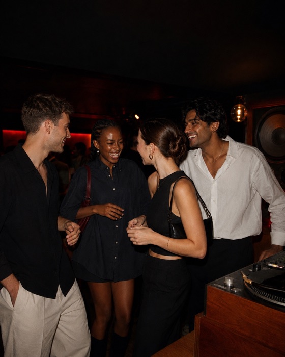 Four friends laughing beside a turntable in a listening bar